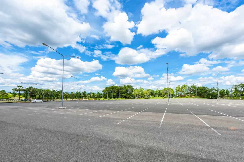 Empty large outdoor parking lot with green trees in background.